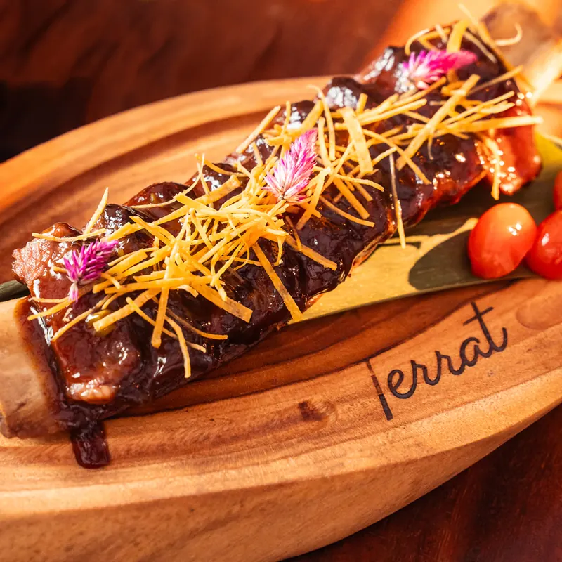 Glazed ribs served on a wooden board with the Terrat logo