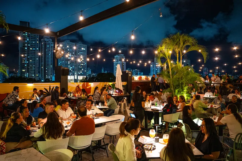 Terrat rooftop at night with palms, string lights and the Panama City skyline